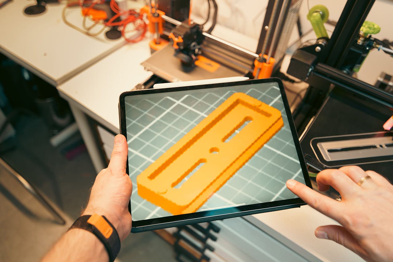 A person uses a tablet to view a 3D model prototype in a workshop equipped with 3D printers.